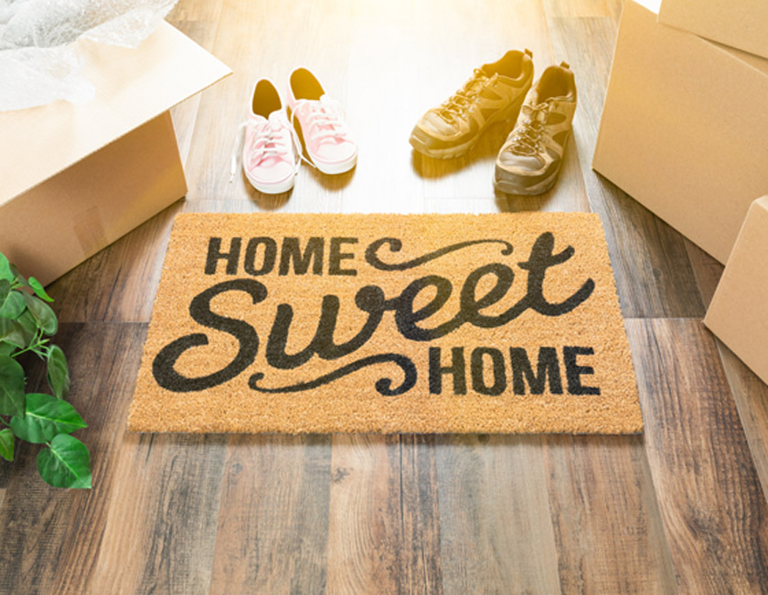 Home-Sweet-Home-Welcome-mat-next-to-moving-boxes-and-shoes-on-hardwood-floors